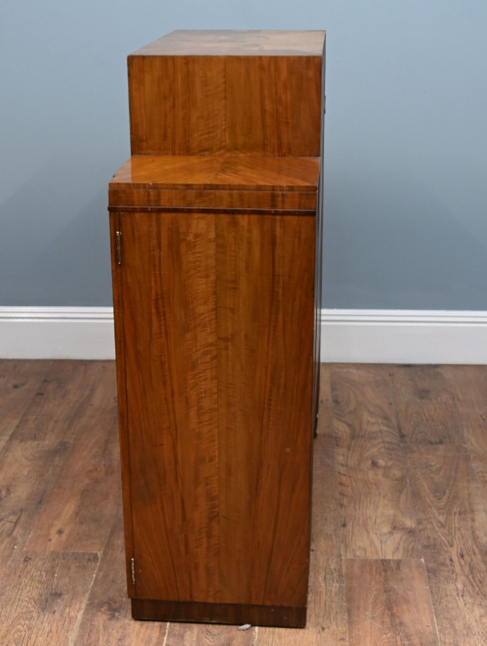 An Art Deco figured walnut display cabinet with a raised central open section containing two glass shelves, flanked by two side cupboards with arched veneer detailing. View VI