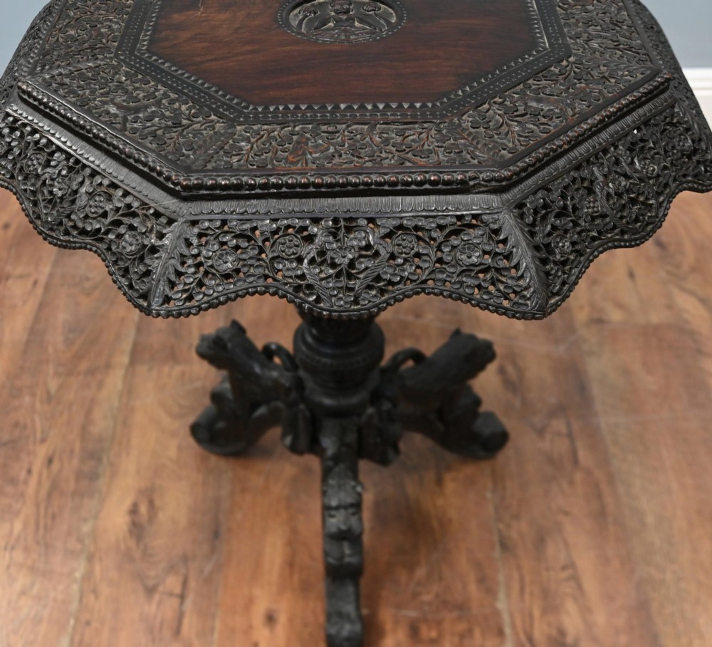 An antique octagonal dark hardwood side table featuring intricate pierced floral carvings around the apron and a central turned pedestal supported by three mythical carved beast legs. View III