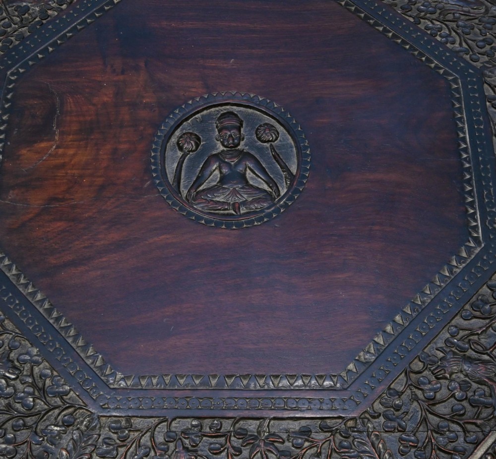 An antique octagonal dark hardwood side table featuring intricate pierced floral carvings around the apron and a central turned pedestal supported by three mythical carved beast legs. View IV