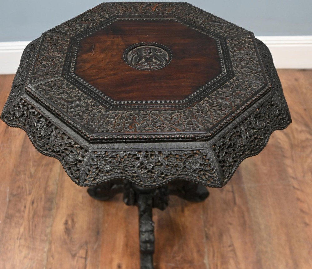 An antique octagonal dark hardwood side table featuring intricate pierced floral carvings around the apron and a central turned pedestal supported by three mythical carved beast legs. View V