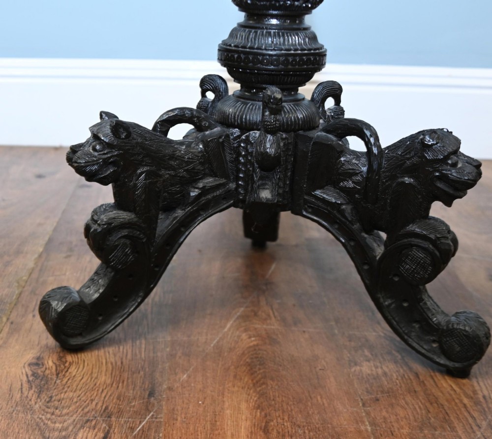 An antique octagonal dark hardwood side table featuring intricate pierced floral carvings around the apron and a central turned pedestal supported by three mythical carved beast legs. View X