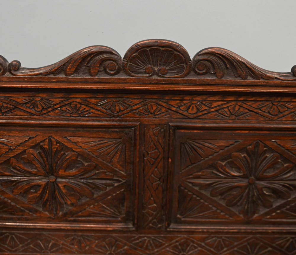 A Victorian dark oak carved settle featuring carved lion head armrests, detailed floral and geometric back panels, and a lift-up storage seat. View III