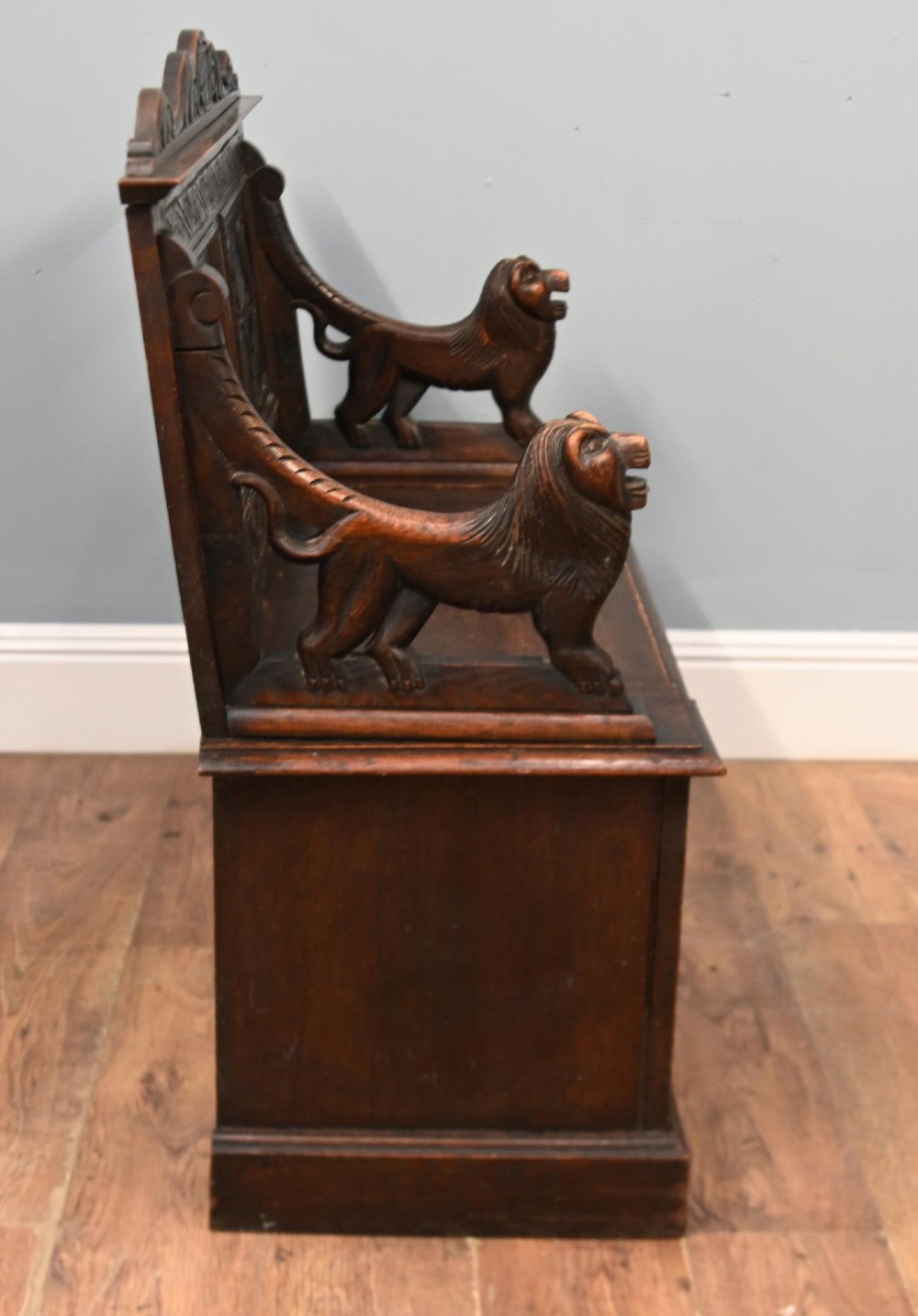 A Victorian dark oak carved settle featuring carved lion head armrests, detailed floral and geometric back panels, and a lift-up storage seat. View VIII