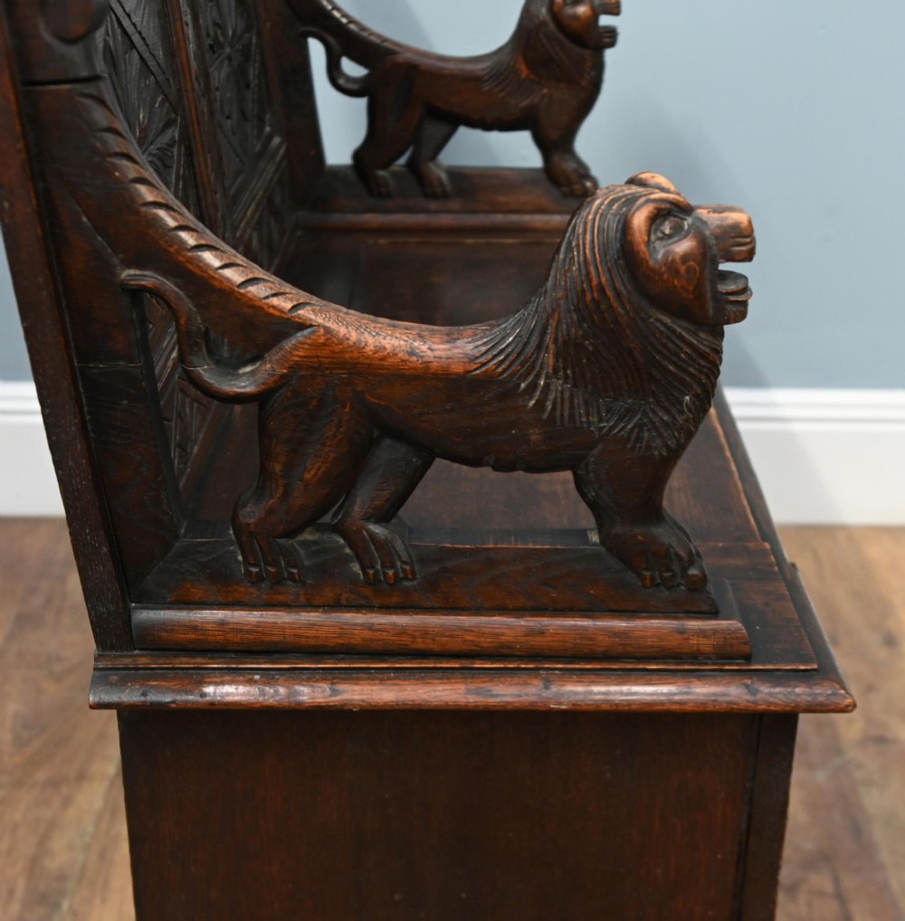 A Victorian dark oak carved settle featuring carved lion head armrests, detailed floral and geometric back panels, and a lift-up storage seat. View X