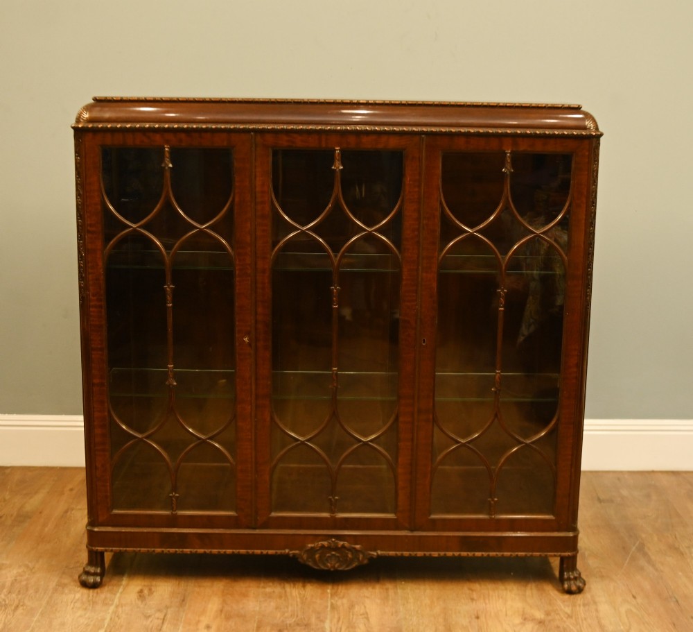 A Chippendale Revival mahogany display cabinet featuring three astragal glazed doors and carved ball and claw feet.