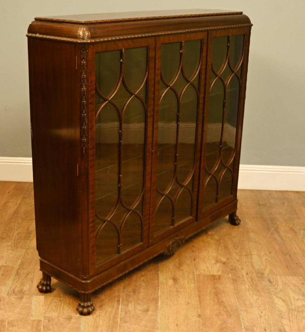 A Chippendale Revival mahogany display cabinet featuring three astragal glazed doors and carved ball and claw feet. View VI