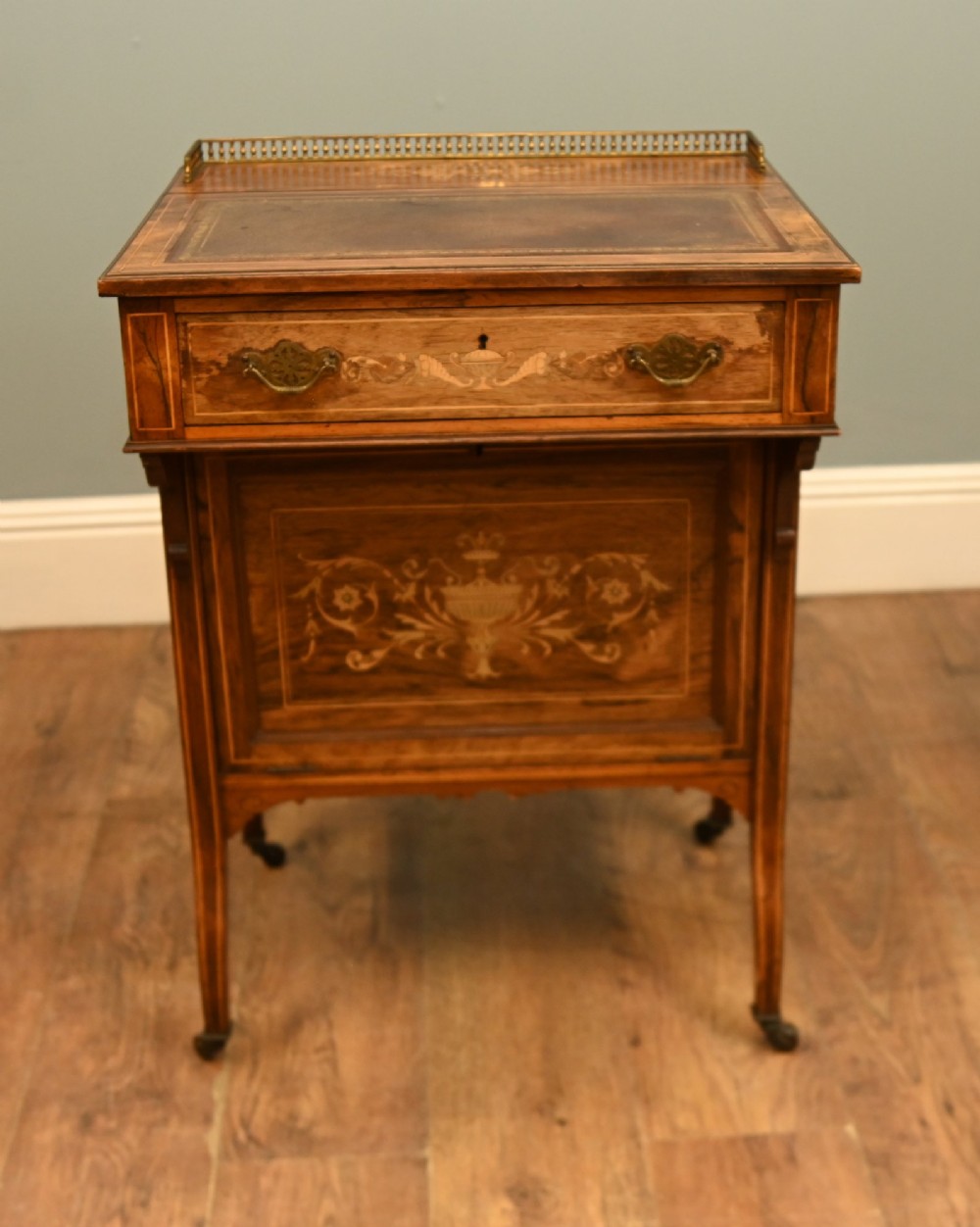 An Edwardian mahogany Davenport desk with urn marquetry inlays, a leather writing slope, brass gallery rim, and legs on castors.