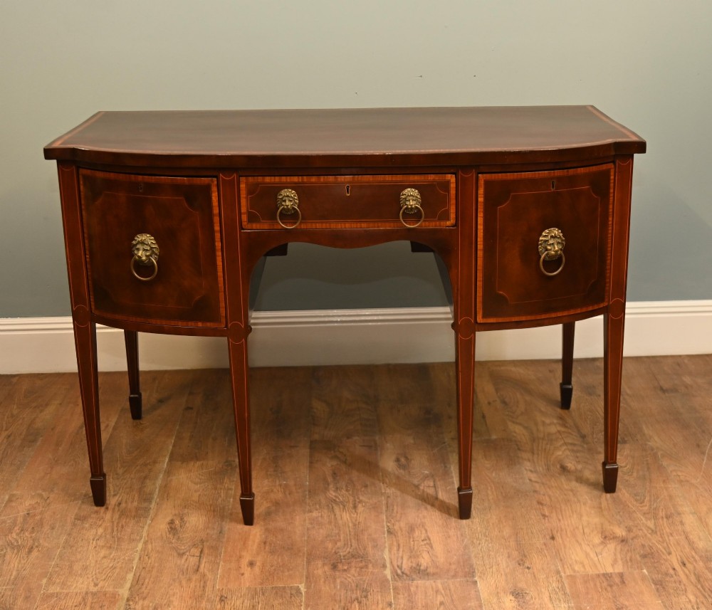 An Edwardian mahogany bowfront sideboard with satinwood inlaid borders, three central drawer and cabinet sections, and brass lion mask ring handles on tapered legs.
