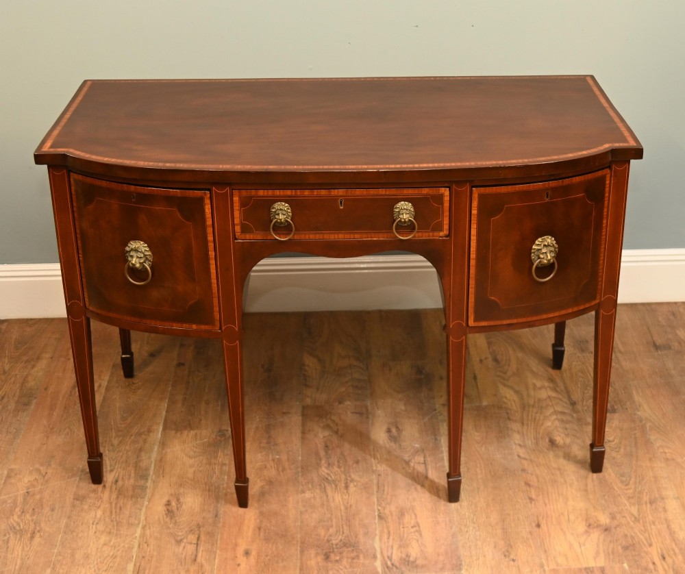 An Edwardian mahogany bowfront sideboard with satinwood inlaid borders, three central drawer and cabinet sections, and brass lion mask ring handles on tapered legs. View III