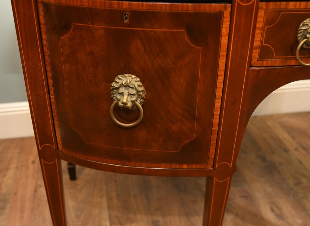 An Edwardian mahogany bowfront sideboard with satinwood inlaid borders, three central drawer and cabinet sections, and brass lion mask ring handles on tapered legs. View IV