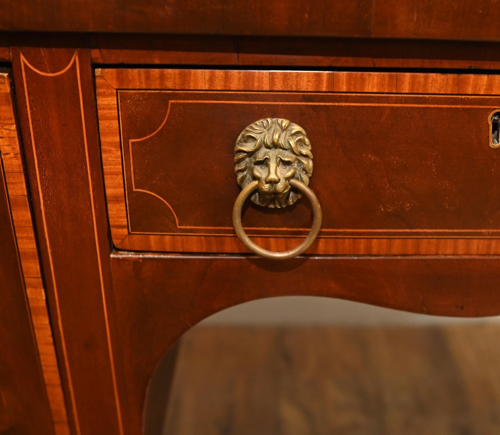 An Edwardian mahogany bowfront sideboard with satinwood inlaid borders, three central drawer and cabinet sections, and brass lion mask ring handles on tapered legs. View V
