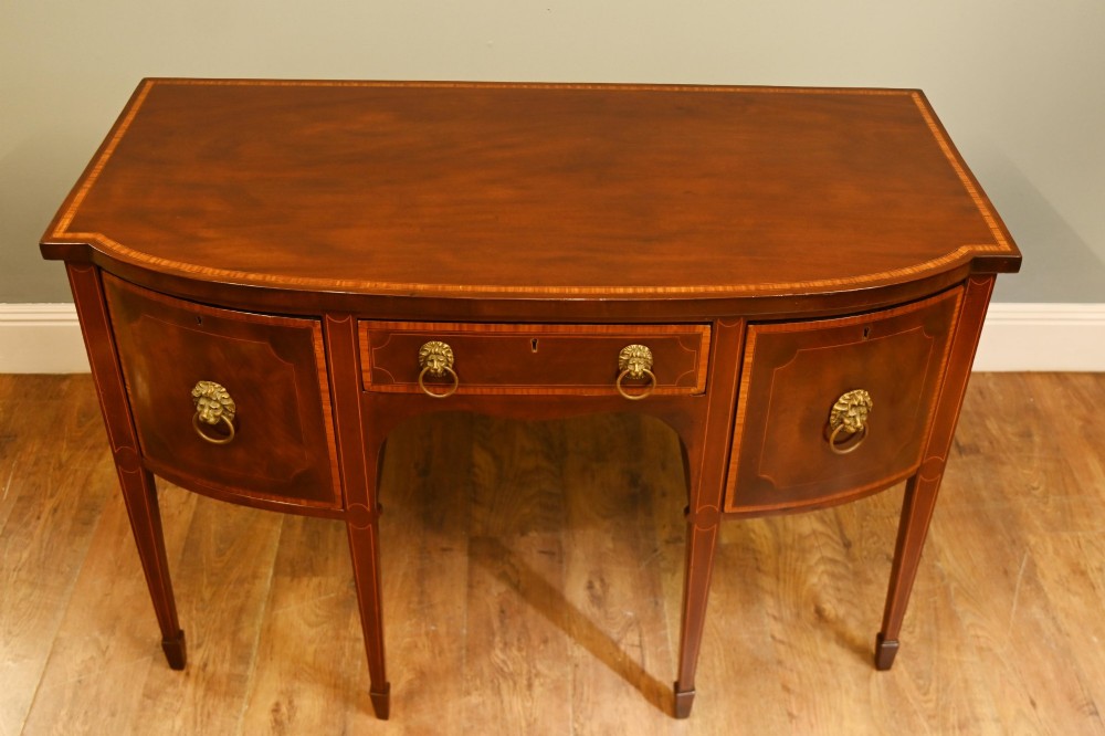 An Edwardian mahogany bowfront sideboard with satinwood inlaid borders, three central drawer and cabinet sections, and brass lion mask ring handles on tapered legs. View VII