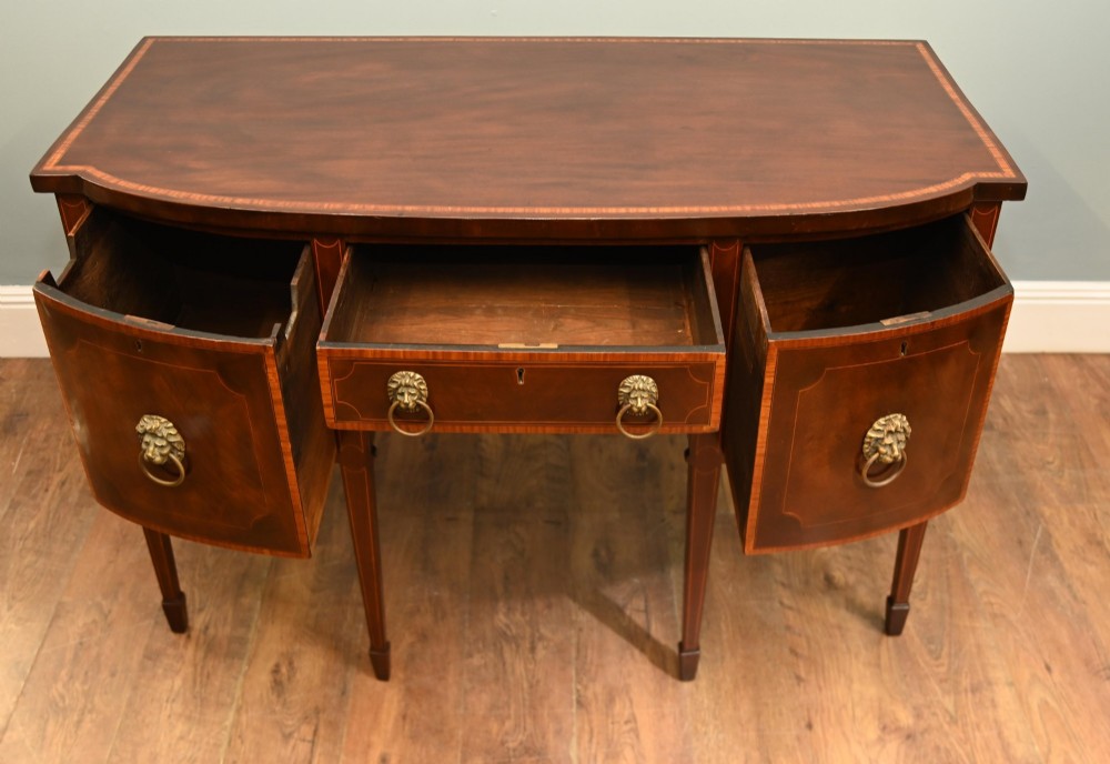 An Edwardian mahogany bowfront sideboard with satinwood inlaid borders, three central drawer and cabinet sections, and brass lion mask ring handles on tapered legs. View VIII