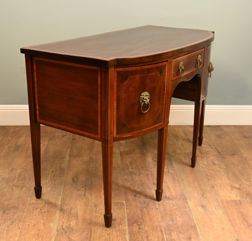 An Edwardian mahogany bowfront sideboard with satinwood inlaid borders, three central drawer and cabinet sections, and brass lion mask ring handles on tapered legs. View IX