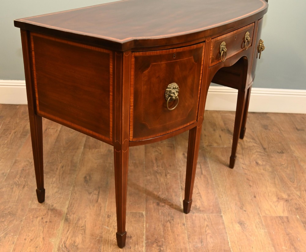 An Edwardian mahogany bowfront sideboard with satinwood inlaid borders, three central drawer and cabinet sections, and brass lion mask ring handles on tapered legs. View X