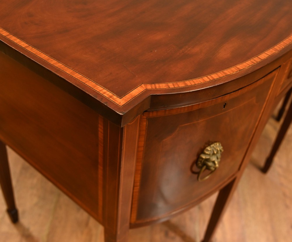 An Edwardian mahogany bowfront sideboard with satinwood inlaid borders, three central drawer and cabinet sections, and brass lion mask ring handles on tapered legs. View XI
