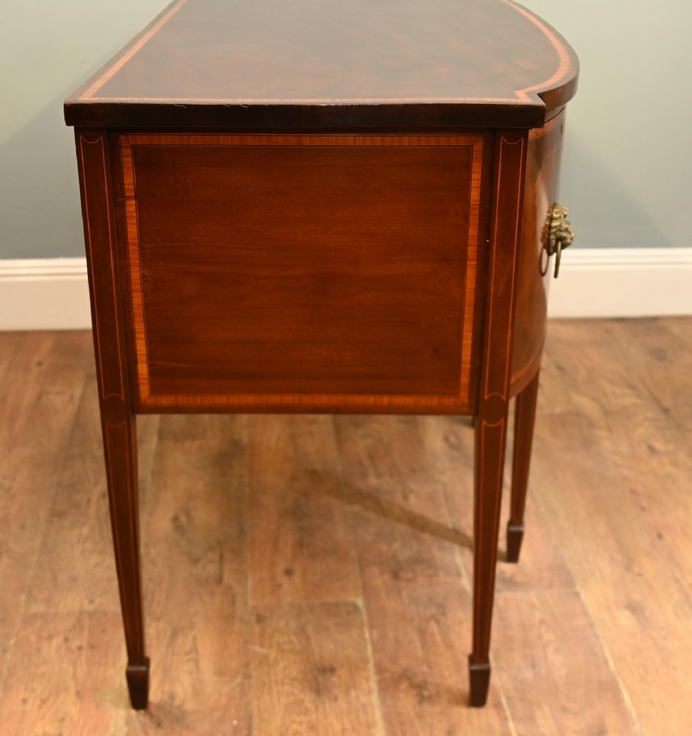 An Edwardian mahogany bowfront sideboard with satinwood inlaid borders, three central drawer and cabinet sections, and brass lion mask ring handles on tapered legs. View XII