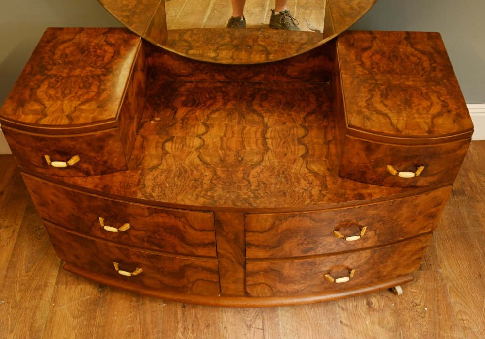 An Art Deco burr walnut dressing table featuring a large circular mirror mounted behind six bow-fronted drawers. View II