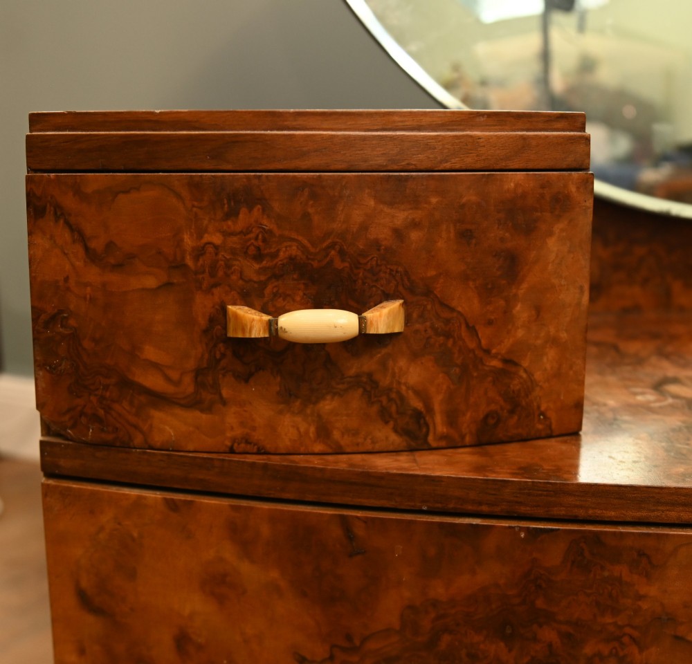 An Art Deco burr walnut dressing table featuring a large circular mirror mounted behind six bow-fronted drawers. View VII