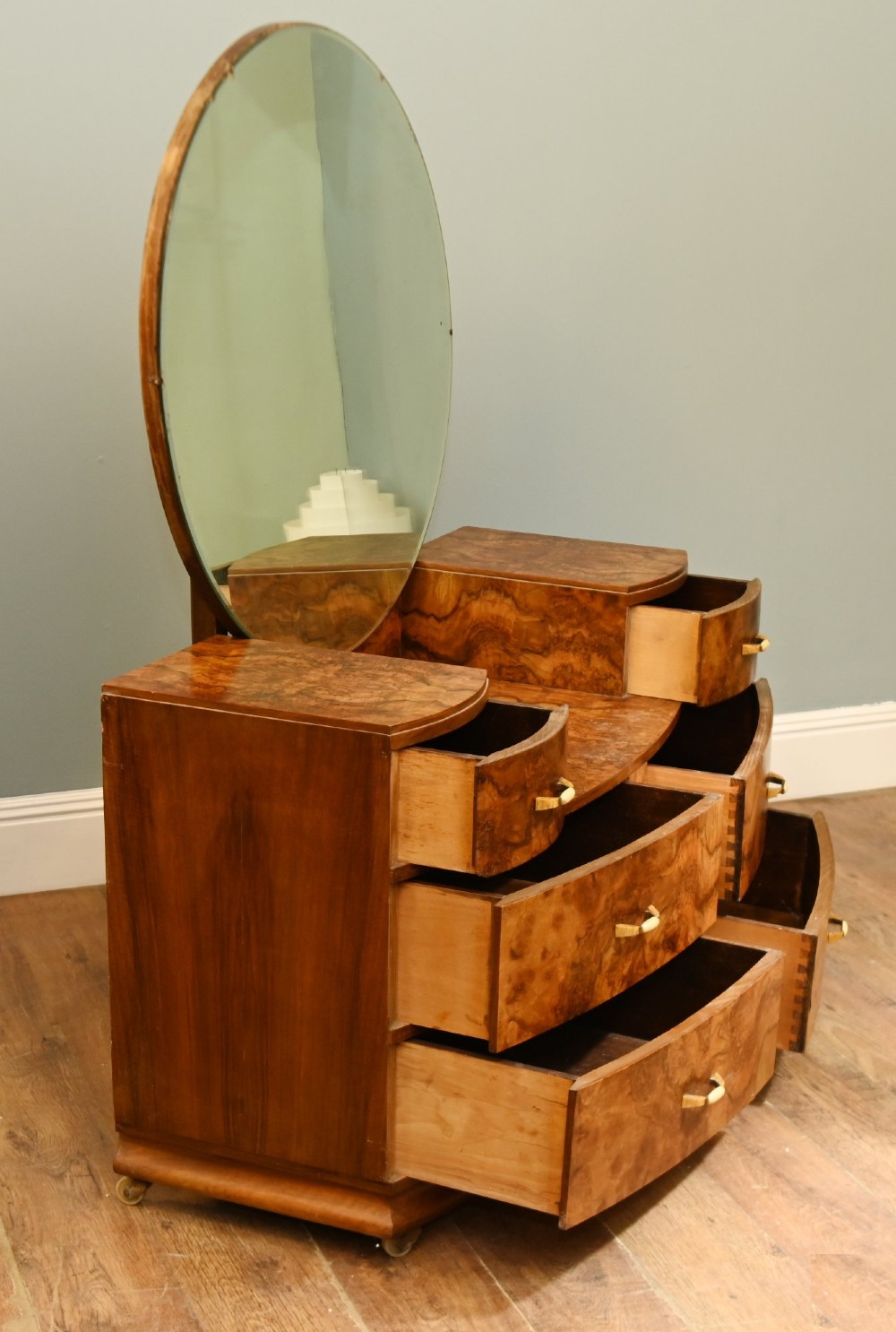 An Art Deco burr walnut dressing table featuring a large circular mirror mounted behind six bow-fronted drawers. View IX