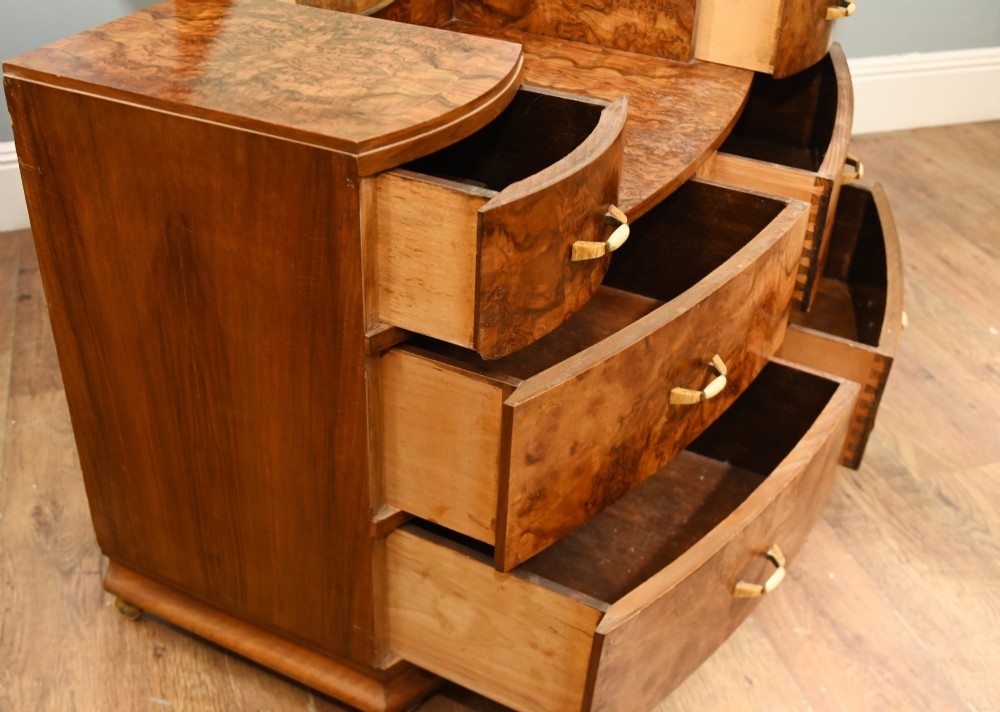 An Art Deco burr walnut dressing table featuring a large circular mirror mounted behind six bow-fronted drawers. View X