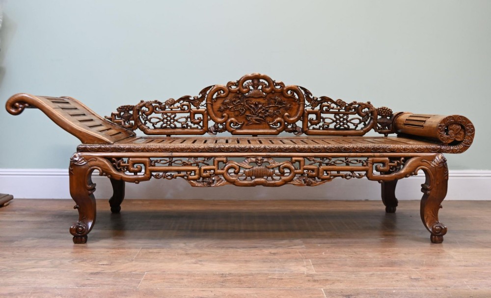 An intricately hand-carved warm brown hardwood Chinese opium bench featuring a slatted seat, elevated recline end, and pierced scrollwork along the backrest. View III