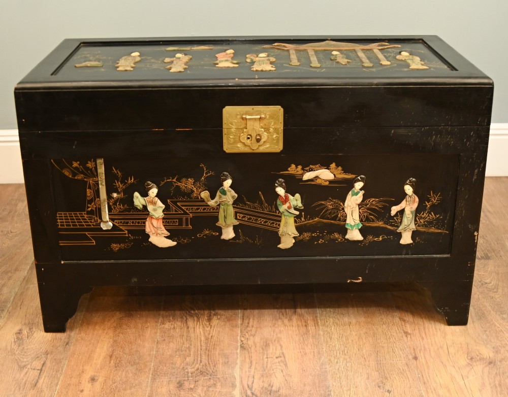 A black lacquered rectangular wooden chest embellished with raised soapstone figures and landscape scenes, fitted with an etched brass lock plate.