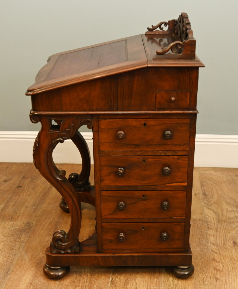A Victorian mahogany Davenport desk featuring a sloped leather writing top, carved cresting rail, serpentine front supports, and side drawers. View VI