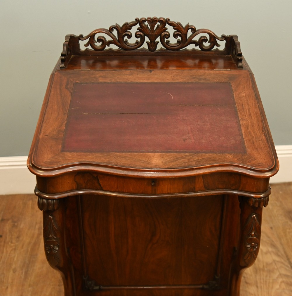 A Victorian mahogany Davenport desk featuring a sloped leather writing top, carved cresting rail, serpentine front supports, and side drawers. View XI