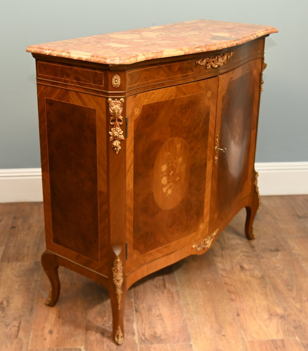 A Louis XV Revival walnut side cabinet featuring a serpentine front, floral marquetry inlay, pink marble top, and gilt-bronze mounts on cabriole legs. View VI