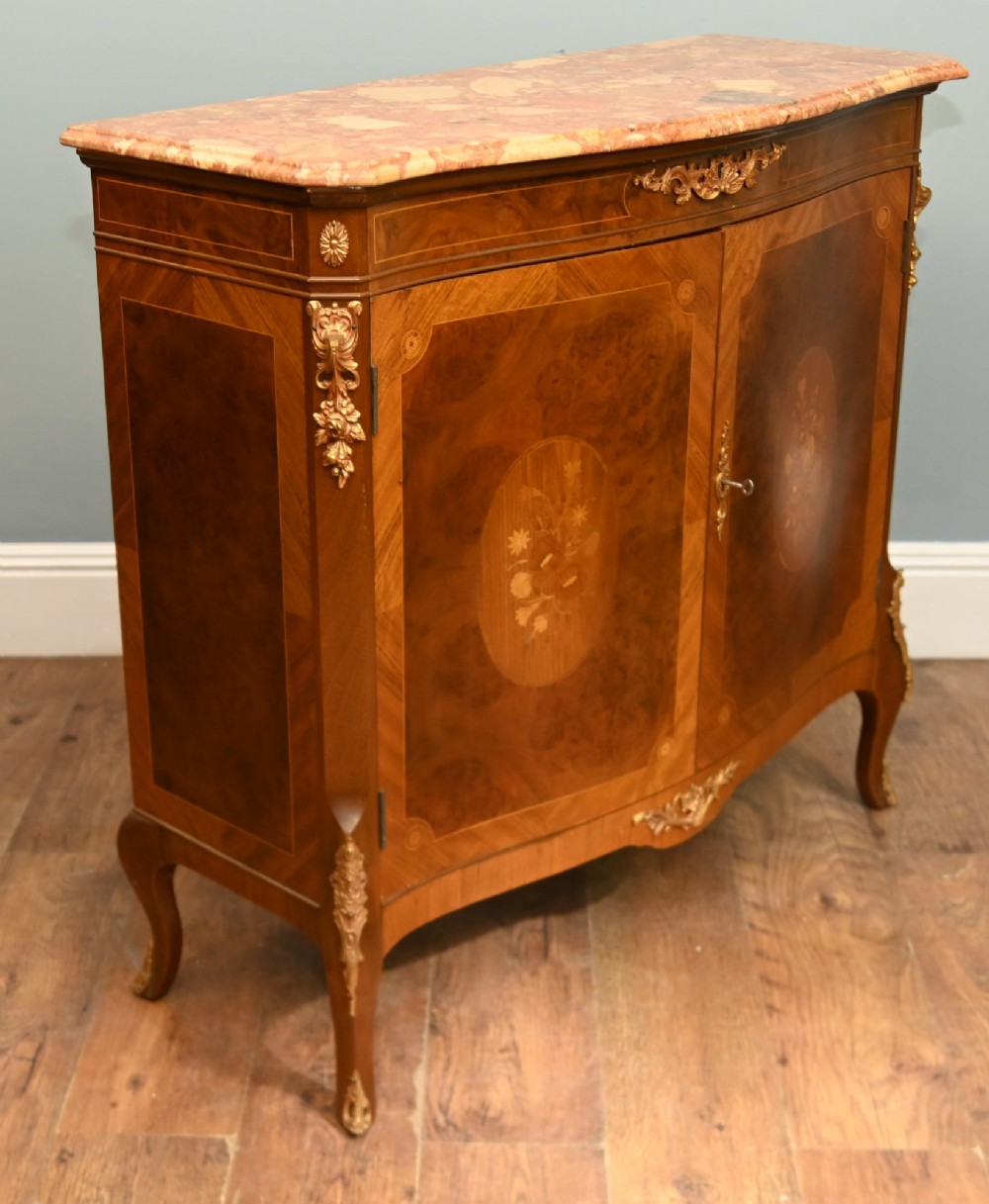 A Louis XV Revival walnut side cabinet featuring a serpentine front, floral marquetry inlay, pink marble top, and gilt-bronze mounts on cabriole legs. View VII