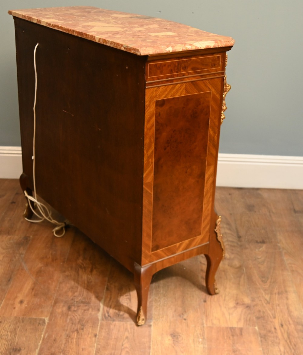 A Louis XV Revival walnut side cabinet featuring a serpentine front, floral marquetry inlay, pink marble top, and gilt-bronze mounts on cabriole legs. View X