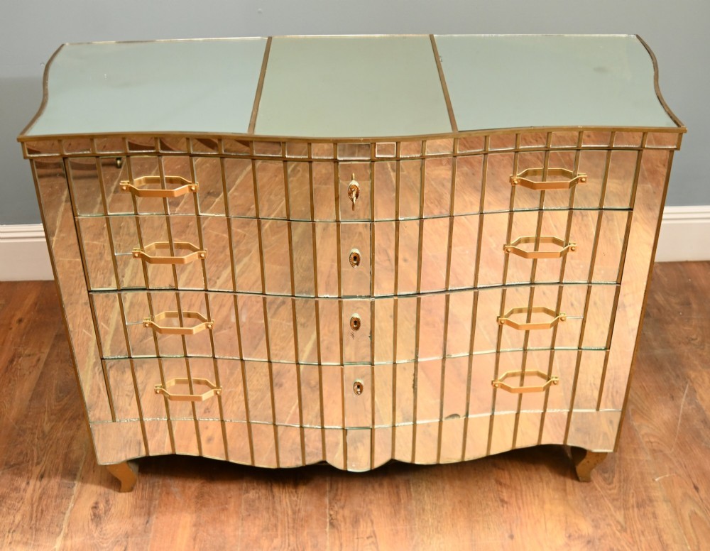 An Art Deco mirrored chest of drawers featuring segmented glass panelling, four drawers with geometric brass handles, and a shaped lower apron. View II