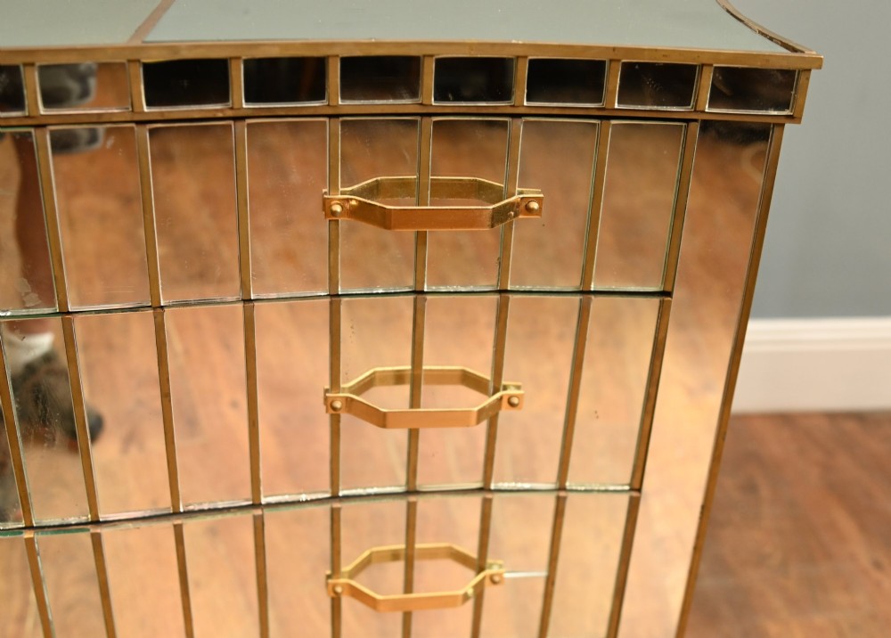 An Art Deco mirrored chest of drawers featuring segmented glass panelling, four drawers with geometric brass handles, and a shaped lower apron. View III
