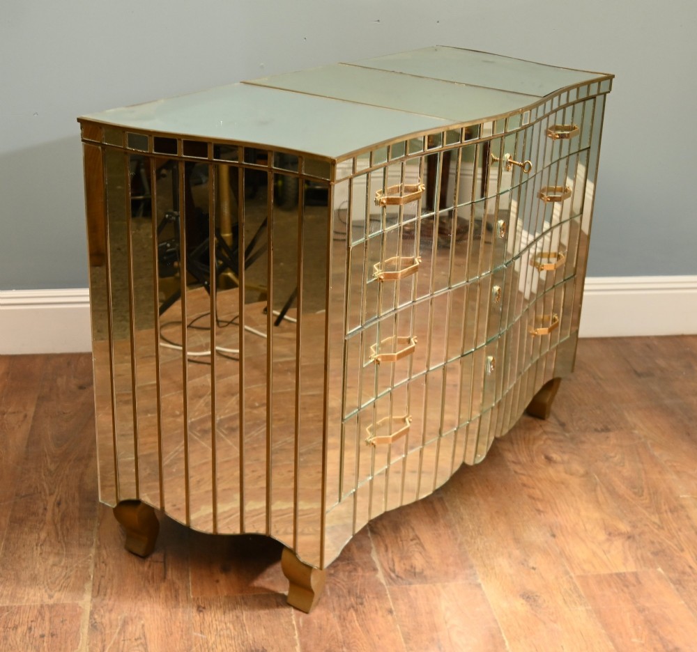 An Art Deco mirrored chest of drawers featuring segmented glass panelling, four drawers with geometric brass handles, and a shaped lower apron. View VI