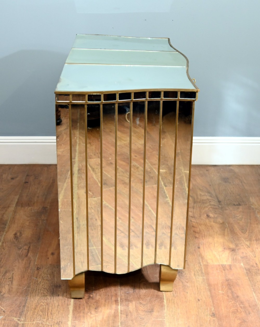 An Art Deco mirrored chest of drawers featuring segmented glass panelling, four drawers with geometric brass handles, and a shaped lower apron. View VIII
