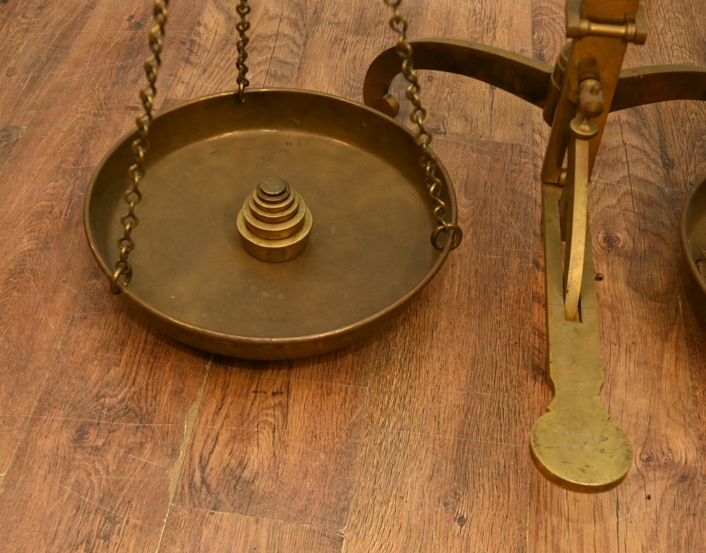 A nineteenth-century brass Avery balance scale featuring a tall central pillar, horizontal beam, twin hanging circular pans, and nested counterweights. View VI
