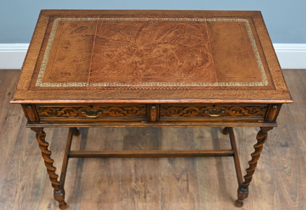 A Victorian oak writing desk featuring barley twist legs, carved apron detailing, a leather inset writing surface, and an H-stretcher. View V