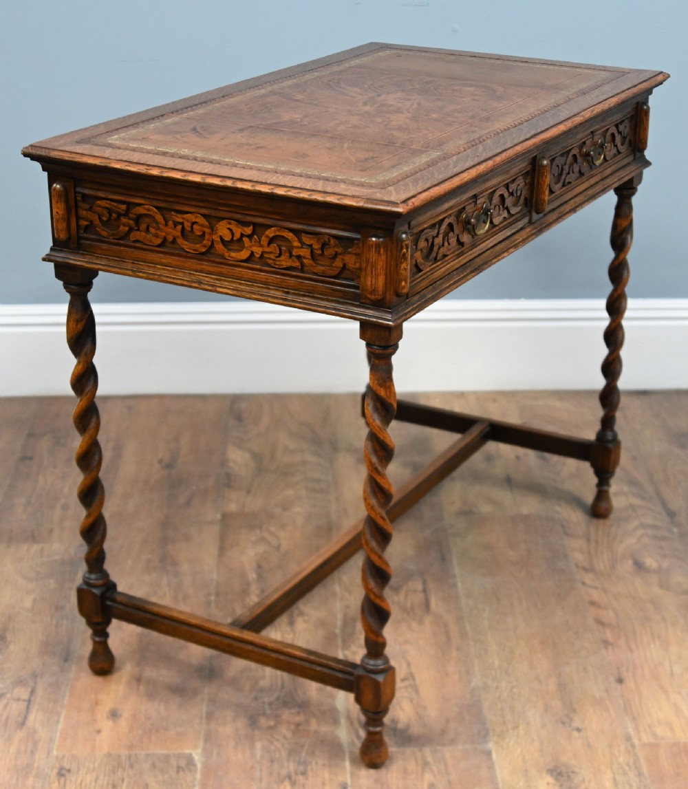 A Victorian oak writing desk featuring barley twist legs, carved apron detailing, a leather inset writing surface, and an H-stretcher.