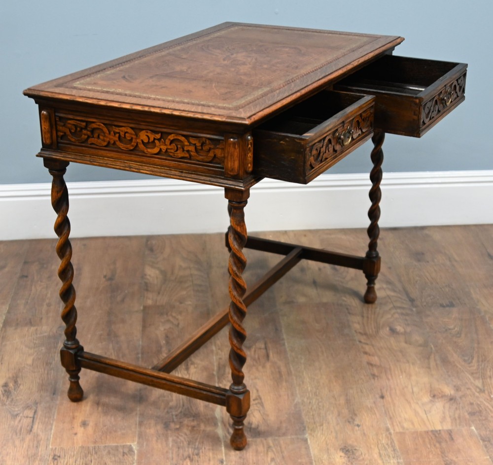 A Victorian oak writing desk featuring barley twist legs, carved apron detailing, a leather inset writing surface, and an H-stretcher. View VI