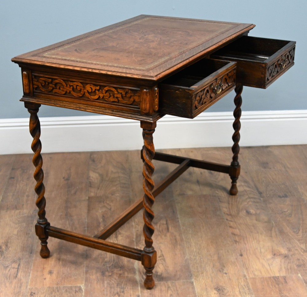 A Victorian oak writing desk featuring barley twist legs, carved apron detailing, a leather inset writing surface, and an H-stretcher. View VII