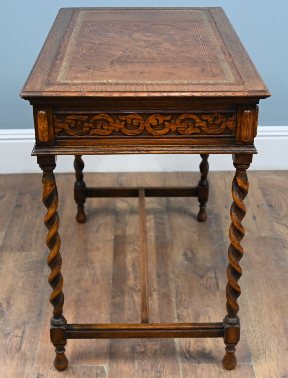 A Victorian oak writing desk featuring barley twist legs, carved apron detailing, a leather inset writing surface, and an H-stretcher. View IX