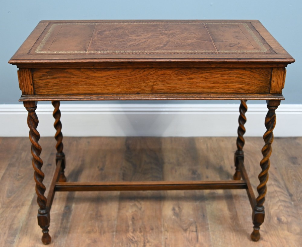 A Victorian oak writing desk featuring barley twist legs, carved apron detailing, a leather inset writing surface, and an H-stretcher. View X