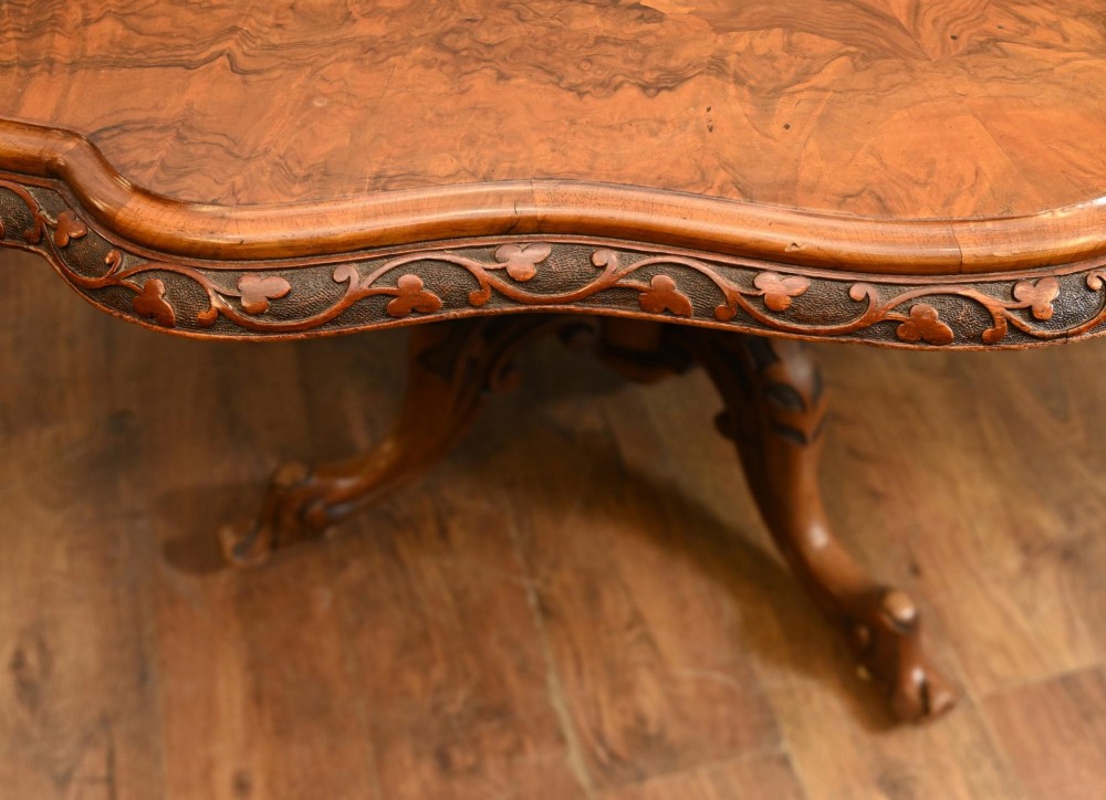 A mid-19th-century Irish burr walnut centre table featuring a shaped serpentine top with a carved frieze set on a turned pedestal with four carved legs. View III