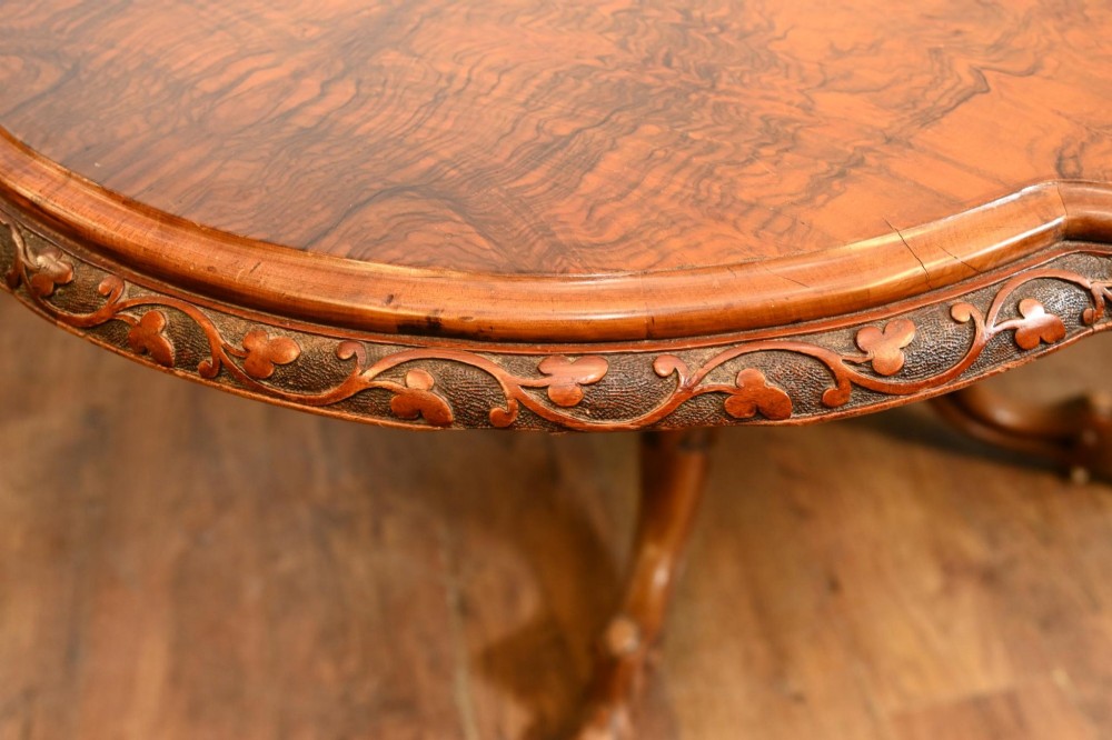 A mid-19th-century Irish burr walnut centre table featuring a shaped serpentine top with a carved frieze set on a turned pedestal with four carved legs. View IV