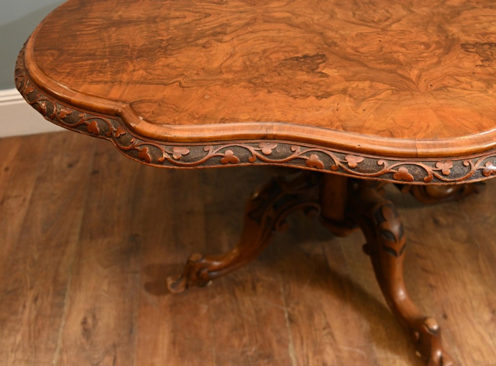 A mid-19th-century Irish burr walnut centre table featuring a shaped serpentine top with a carved frieze set on a turned pedestal with four carved legs. View V