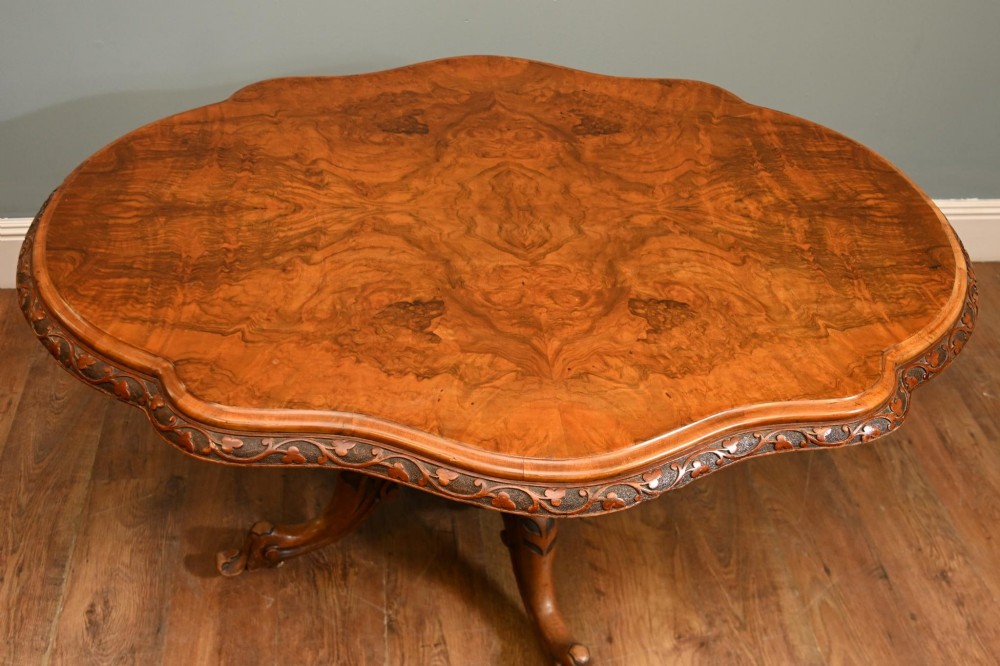A mid-19th-century Irish burr walnut centre table featuring a shaped serpentine top with a carved frieze set on a turned pedestal with four carved legs. View VI