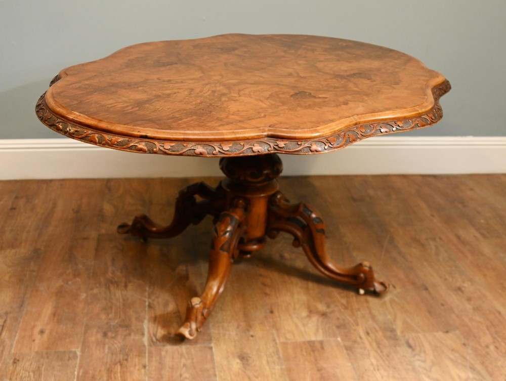 A mid-19th-century Irish burr walnut centre table featuring a shaped serpentine top with a carved frieze set on a turned pedestal with four carved legs.
