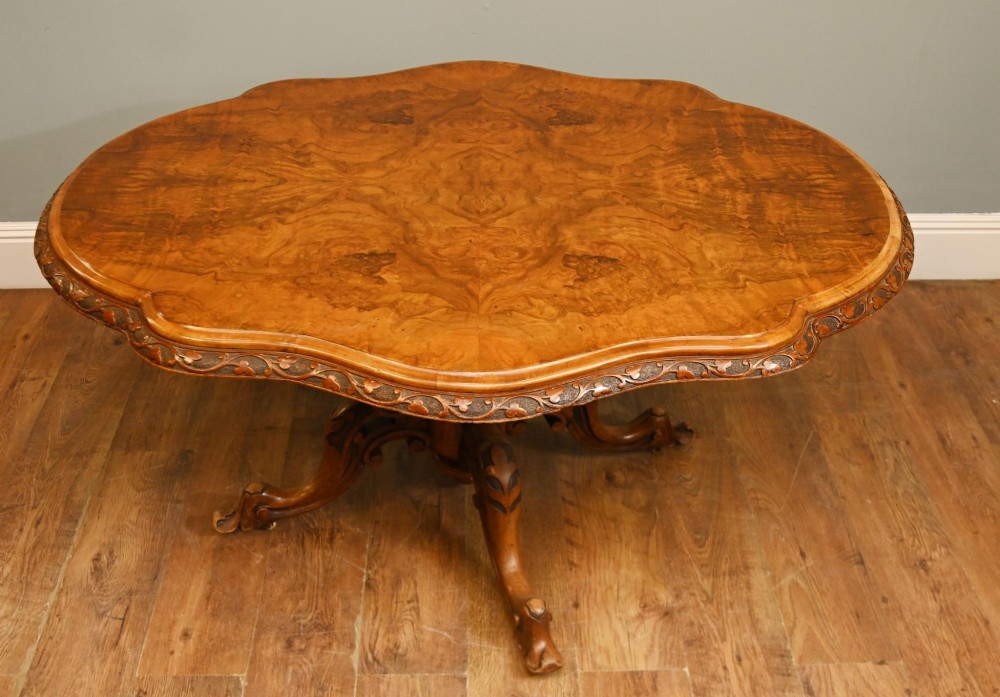 A mid-19th-century Irish burr walnut centre table featuring a shaped serpentine top with a carved frieze set on a turned pedestal with four carved legs. View X