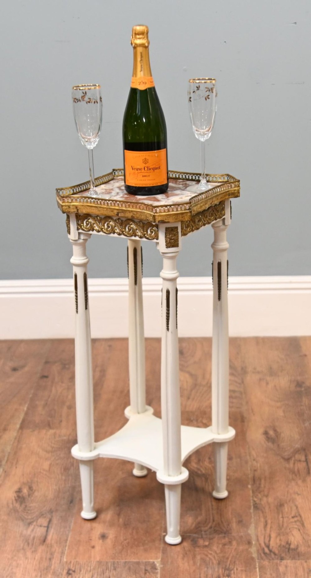 A white painted tall French pedestal stand featuring four fluted legs, gilt brass mounts, a lower tier, and a shaped variegated marble top with a brass gallery. View II